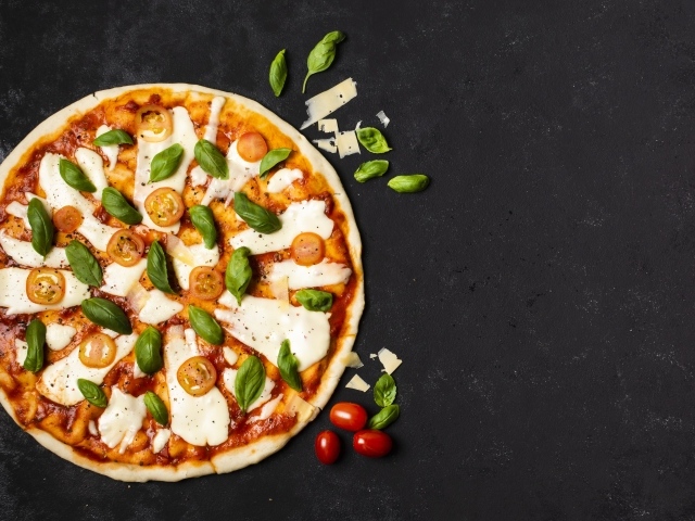 Пицца с сыром, базиликом и помидорами на черном столе 