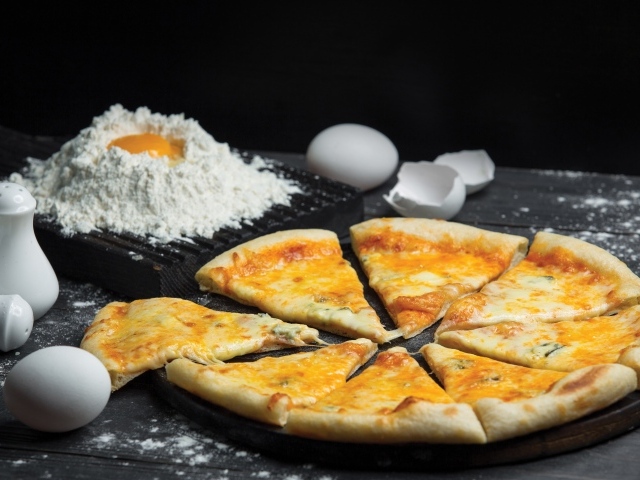 Пицца с сыром нарезана кусочками на столе с мукой и яйцами
