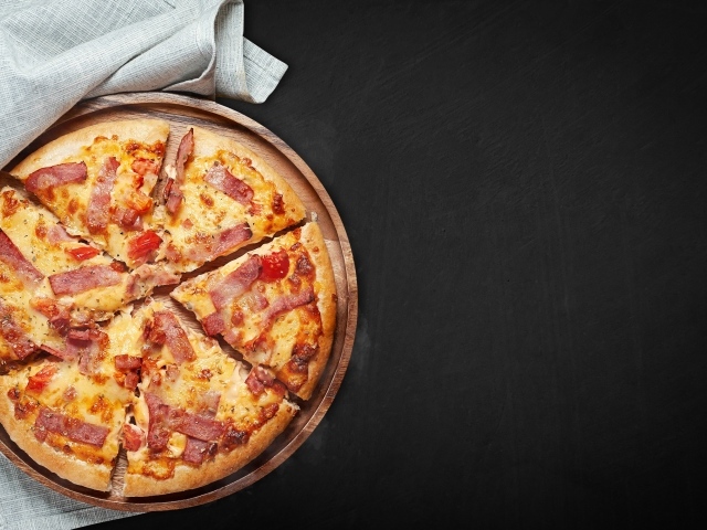 Пицца с кусочками бекона на доске на черном фоне