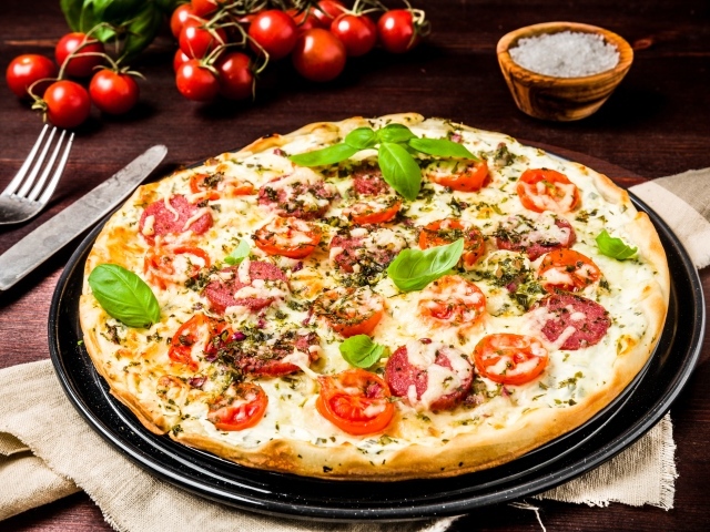 Вкусная пицца с колбасой, сыром и помидорами на столе 