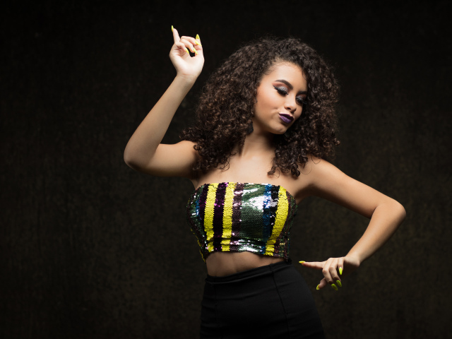 Девушка в ярком топе и черной юбке танцует у стены