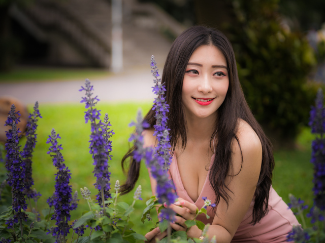 Улыбающаяся азиатка стоит у синих цветов 