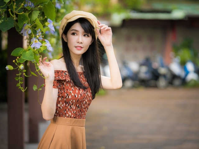 Молодая девушка азиатка в кепке стоит у голубых цветов