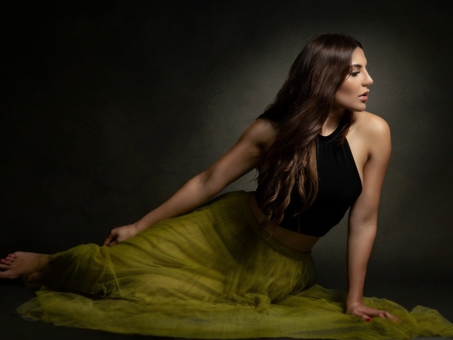 Молодая девушка в длинной юбке сидит на полу