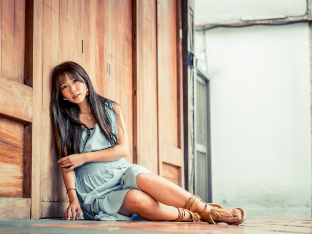 Девушка азиатка в платье сидит на полу у стены 