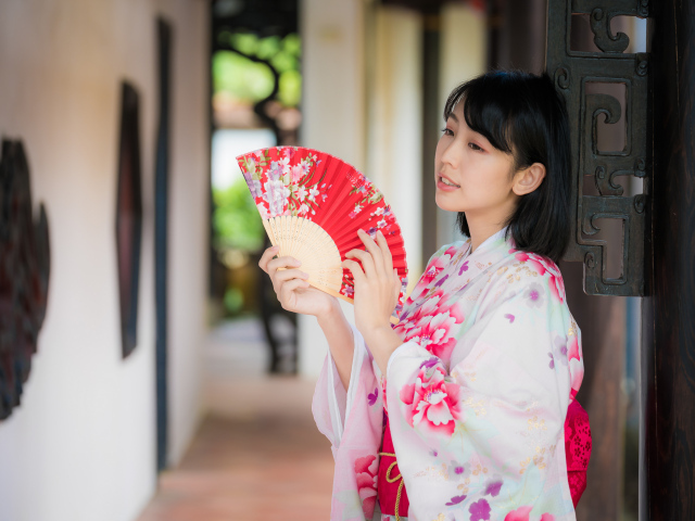 Девушка азиатка в кимоно с веером в руке стоит у ворот 