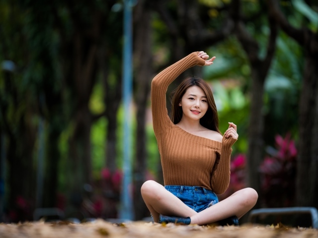 Девушка азиатка сидит в позе лотоса в парке 
