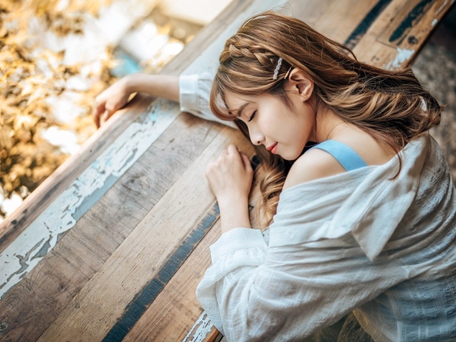Девушка азиатка спит на деревянном столе 
