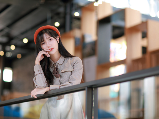 Азиатка в сером платье стоит у перил 