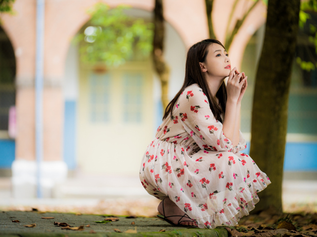 Красивая девушка азиатка в платье сидит под деревом в парке