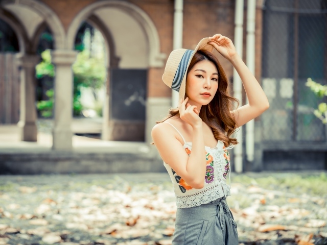 Красивая девушка азиатка в шляпе стоит в парке 