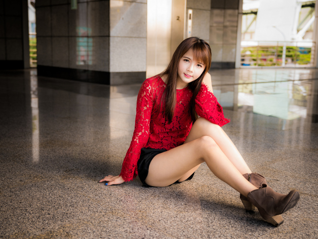 Красивая девушка азиатка в красной блузке сидит на полу