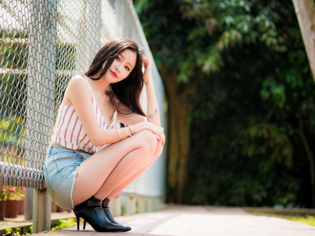 Красивая девушка азиатка сидит у железной сетки