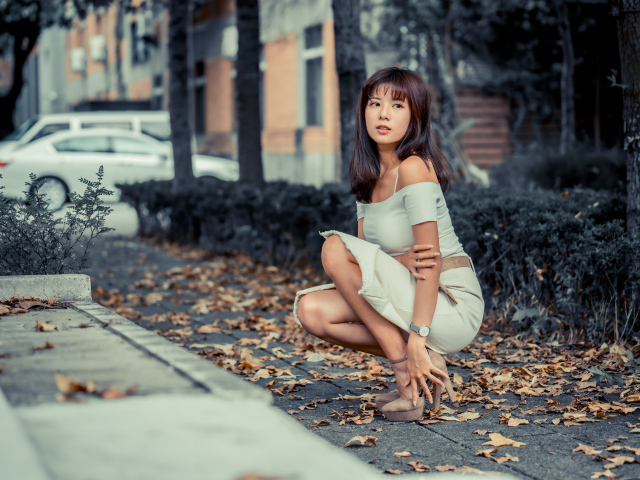 Красивая девушка азиатка в белом платье сидит в осеннем парке 