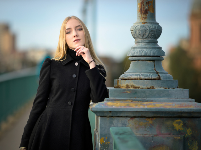 Красивая блондинка в черном пальто стоит у фонаря