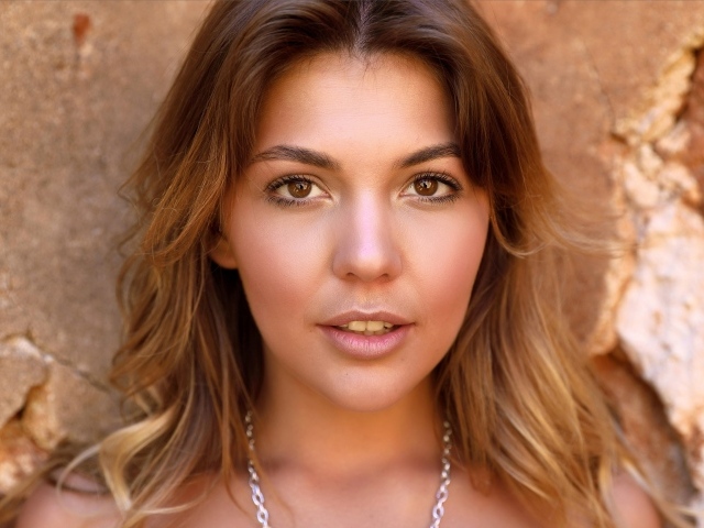 Красивая кареглазая девушка стоит у стены 