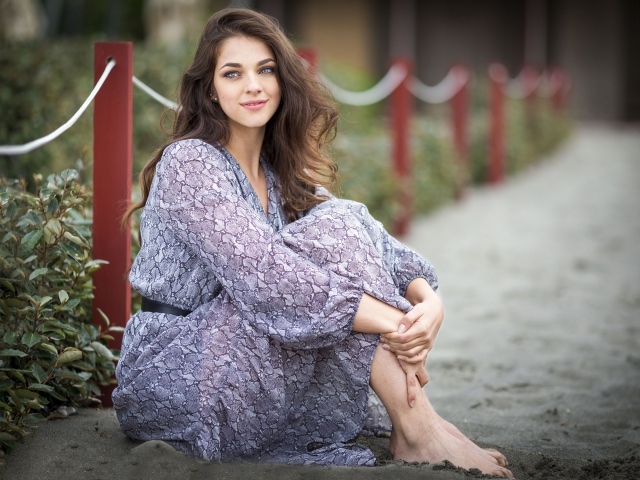 Красивая девушка в платье сидит на песке