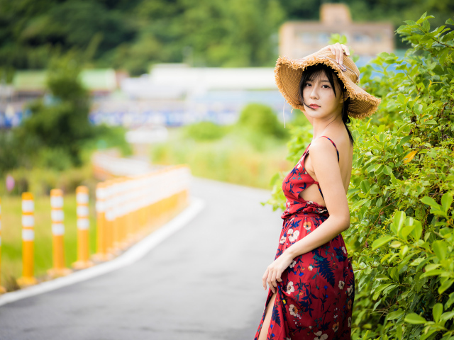 Красивая девушка в сарафане со шляпой на голове у куста 