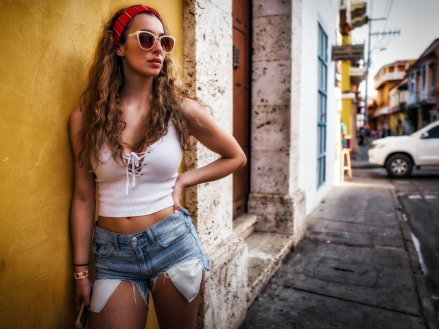 Красивая девушка в солнечных очках стоит у стены