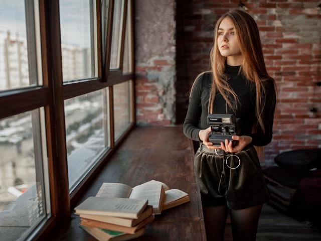 Красивая девушка с фотоаппаратом в руках у окна 