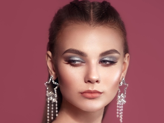 Красивая девушка с макияжем и большими серьгами на розовом фоне