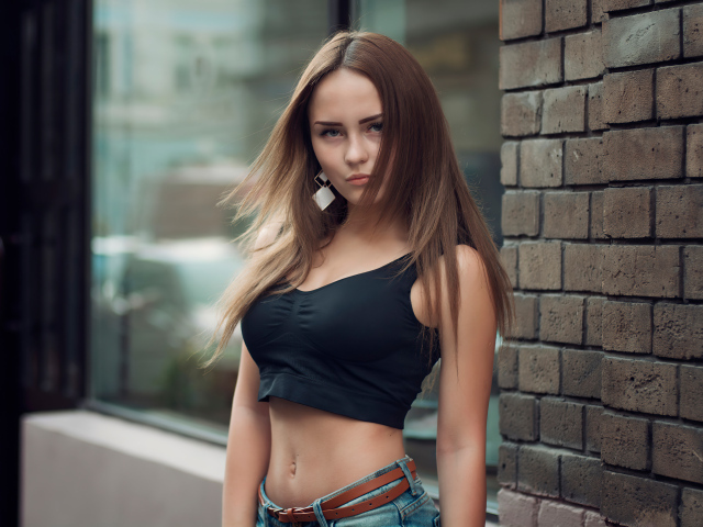 Красивая стройная девушка в черном топе стоит у стены