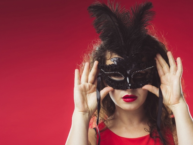 Красивая женщина в черной маске на красном фоне