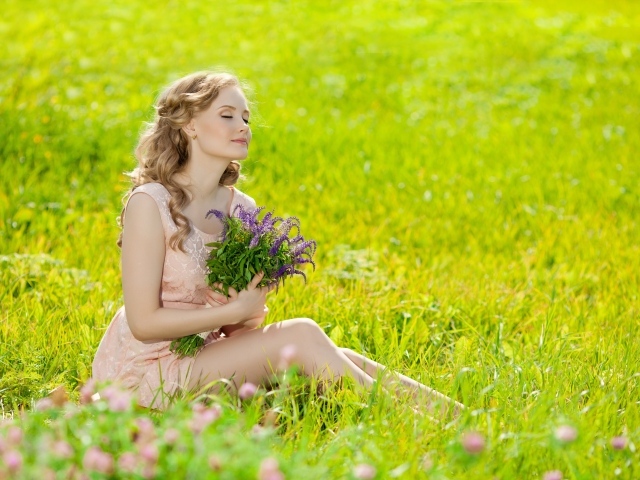 Красивая молодая девушка с букетом цветов сидит на зеленой траве