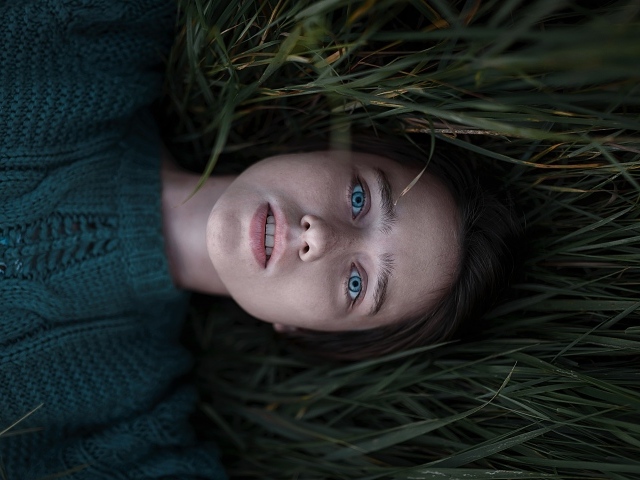 Голубоглазая девушка в свитере лежит на траве