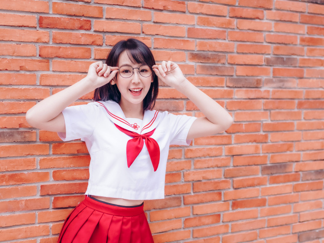 Яркая веселая азиатка в очках у кирпичной стены