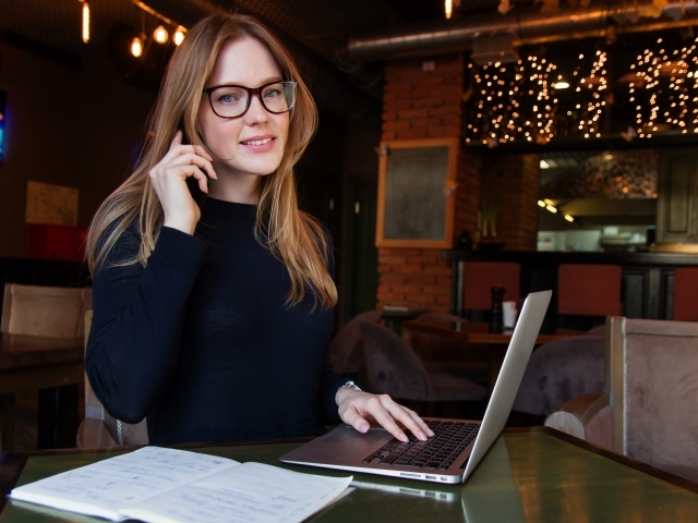 Деловая девушка в очках сидит с кафе с ноутбуком
