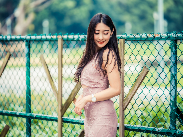 Милая азиатка в платье стоит под забором