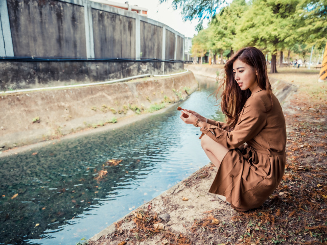 Мечтательная девушка азиатка сидит у воды