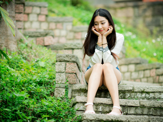 Мечтательная девушка азиатка сидит на ступеньках 