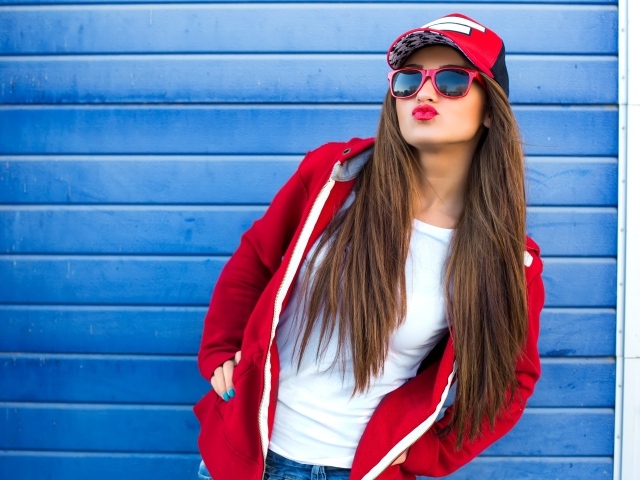 Девушка в бейсболке и солнечных очках у стены