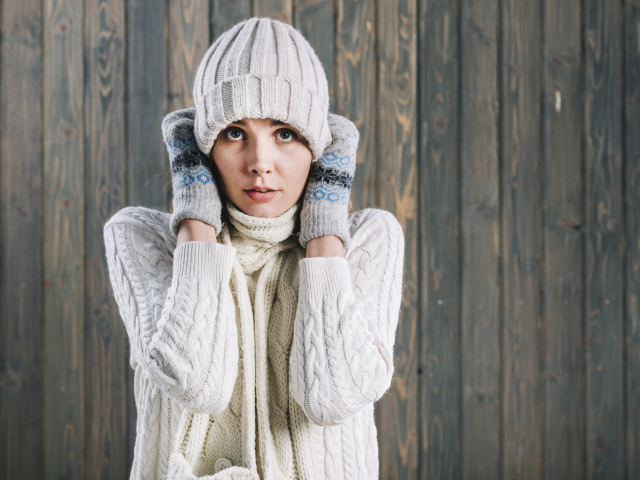 Девушка в варежках поправляет шапку на голове