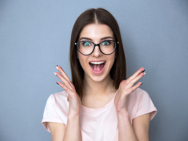 Радостная девушка в очках на сером фоне