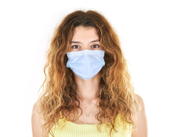 Длинноволосая девушка в маске от коронавируса на белом фоне