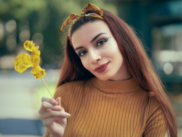 Длинноволосая девушка в свитере с леденцом в руке