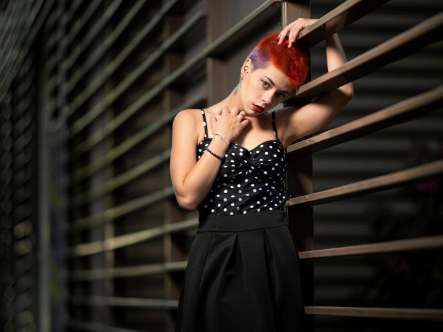 Эпатажная девушка с короткой стрижкой стоит у забора 