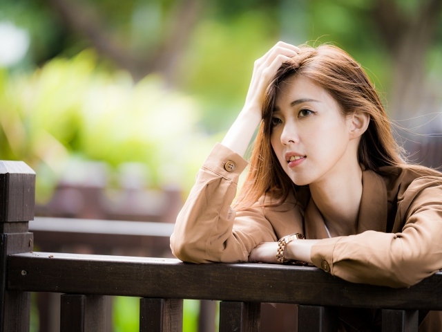 Грустная девушка азиатка стоит у деревянных перил 