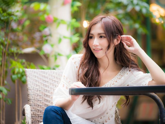 Улыбающаяся девушка азиатка сидит за столом в кафе