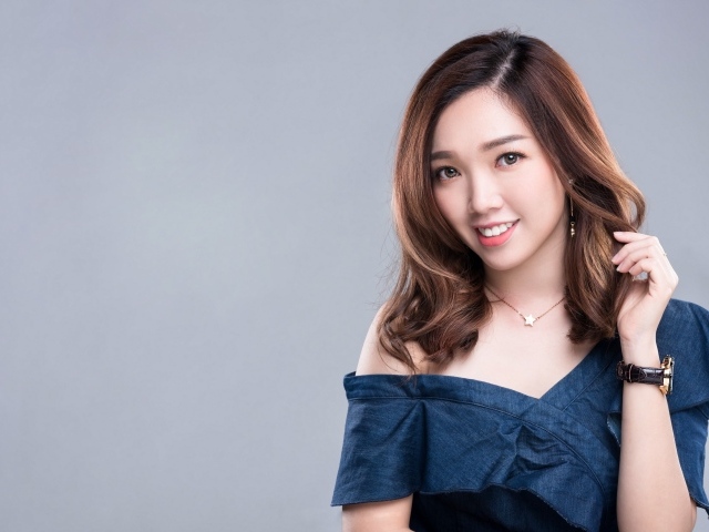 Улыбающаяся девушка азиатка с часами на руке на сером фоне