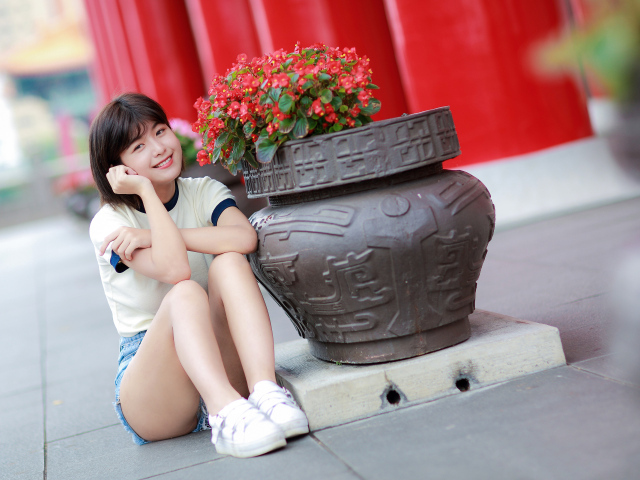 Улыбающаяся азиатка сидит у клумбы с цветами