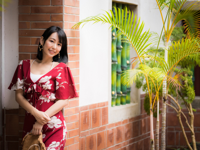 Улыбающаяся азиатка в красном платье стоит у стены 