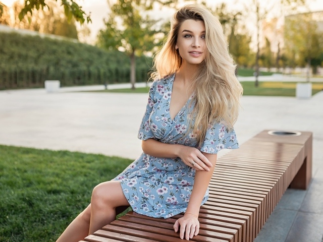 Улыбающаяся блондинка сидит на лавке 