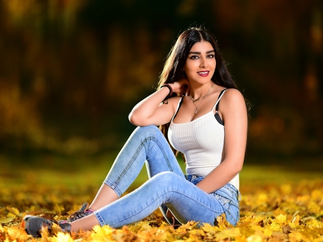 Улыбающаяся брюнетка сидит на опавшей листве