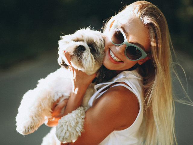 Улыбающаяся девушка в солнечных очках с собакой на руках