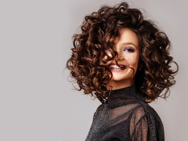 Улыбающаяся девушка с  волнистыми волосами на сером фоне