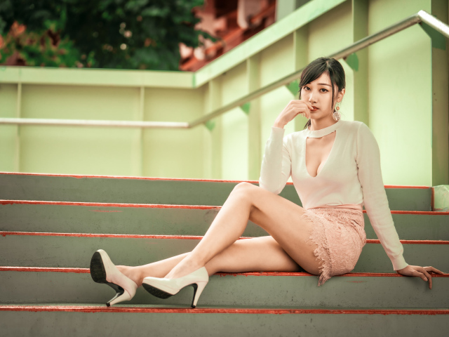Стильная азиатка в туфлях сидит на ступеньках 